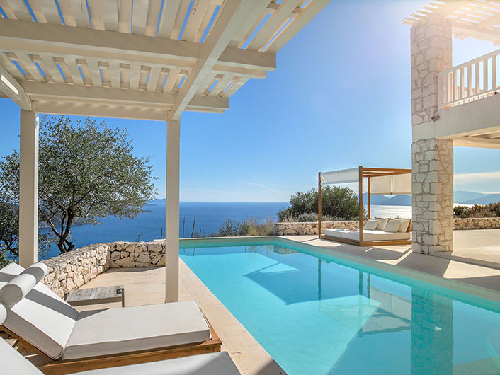 Pool view with the wooden premium sunbeds, the cabana at the end and the sea.